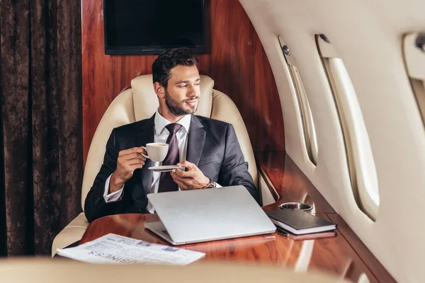 Bel homme d'affaires en costume tenant une tasse de café dans un avion privé — Photo de stock