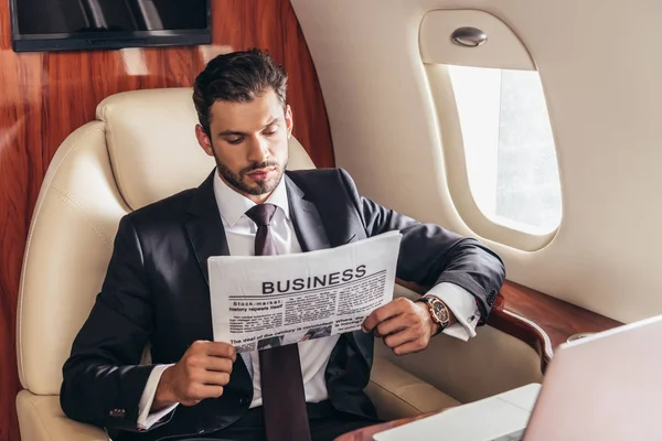Handsome businessman in suit reading newspaper business in private plane — Stock Photo
