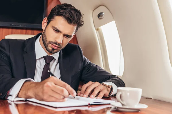 Homem de negócios bonito em terno escrevendo em notebook em avião particular — Fotografia de Stock