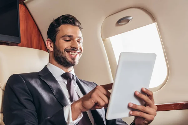 Homme d'affaires souriant en costume en utilisant une tablette numérique dans un avion privé — Photo de stock