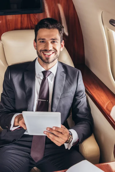 Усміхнений бізнесмен у костюмі тримає цифровий планшет у приватному літаку — стокове фото