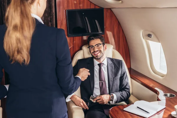 Smiling businessman in suit looking at flight attendant in private plane — Stock Photo