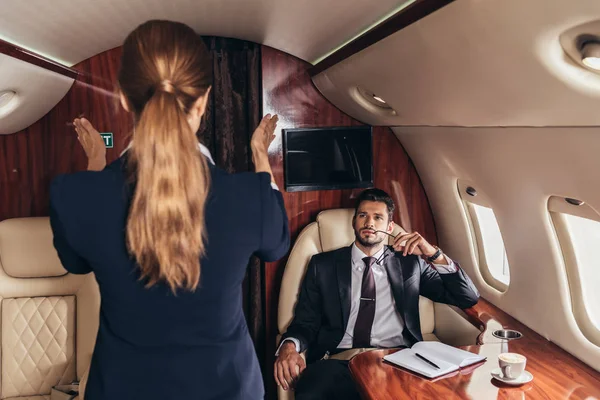 Красивий бізнесмен у костюмі, дивлячись на стюардесу в приватному літаку — стокове фото