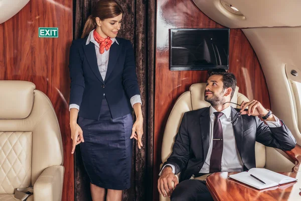 Красивий бізнесмен у костюмі, дивлячись на стюардесу в приватному літаку — стокове фото