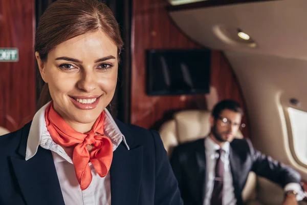 Избирательный фокус улыбающейся и привлекательной стюардессы, смотрящей в камеру в частном самолете — стоковое фото