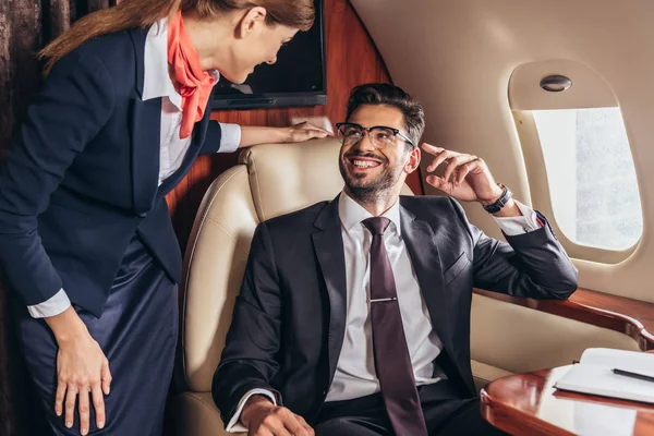 Homme d'affaires souriant en costume regardant l'agent de bord dans un avion privé — Photo de stock