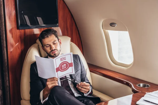 Homem de negócios bonito em terno olhando para o menu em avião privado — Fotografia de Stock