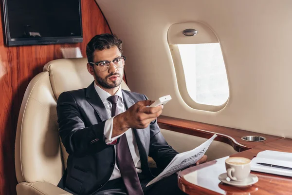 Красивый бизнесмен в костюме держит пульт дистанционного управления в частном самолете — стоковое фото