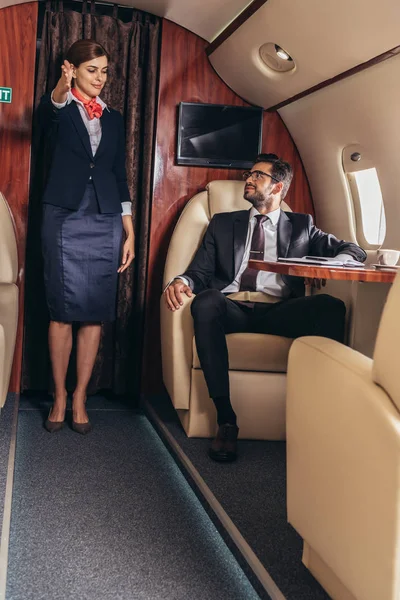 Flight attendant showing gesture to handsome businessman in suit in private plane — Stock Photo