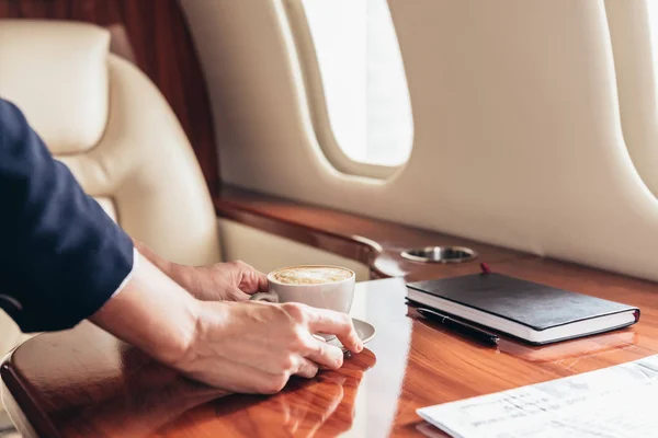 Vista cortada do comissário de bordo colocando xícara de café na mesa em avião privado — Fotografia de Stock