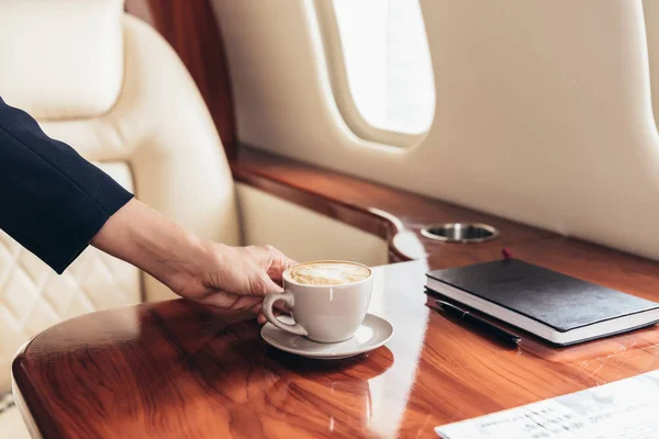 Vista ritagliata di assistente di volo mettendo tazza di caffè sul tavolo in aereo privato — Foto stock