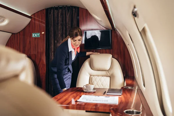 Selective focus of flight attendant in uniform looking down in private plane — Stock Photo