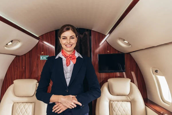 Atendente de voo sorridente de uniforme olhando para a câmera em avião privado — Fotografia de Stock