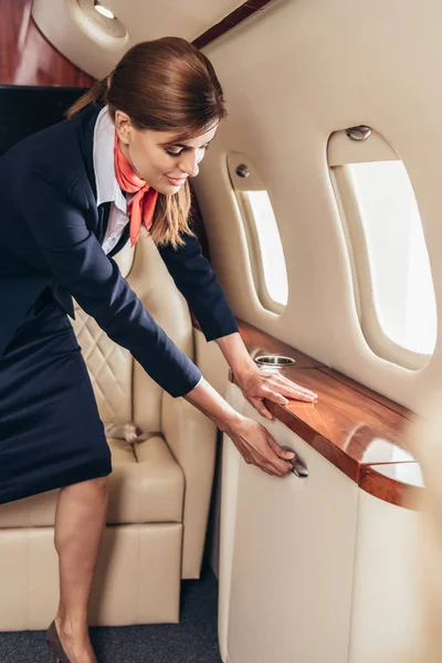Comissária de bordo em alça de retenção uniforme em avião privado — Fotografia de Stock