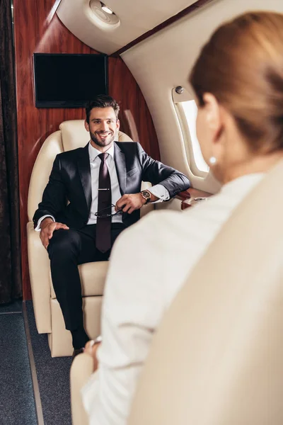 Вибірковий фокус усміхненого бізнесмена, який дивиться на бізнес-леді в приватному літаку — стокове фото