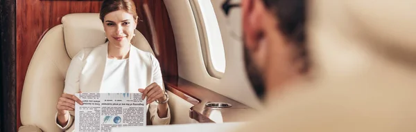 Panoramic shot of smiling businesswoman holding newspaper in private plane — Stock Photo