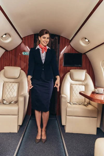 Smiling flight attendant in uniform showing gestures in private plane — Stock Photo