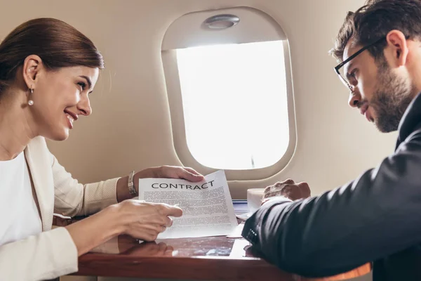 Hombre de negocios y mujer de negocios sonriente mirando contrato en avión privado - foto de stock