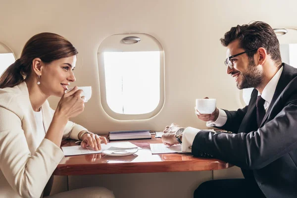 Homme d'affaires souriant et femme d'affaires buvant du café dans un avion privé — Photo de stock