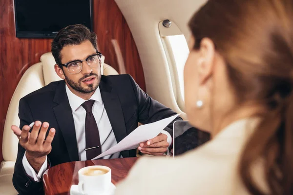 Избирательный фокус бизнесмена, смотрящего на деловую женщину и держащего бумагу в частном самолете — стоковое фото