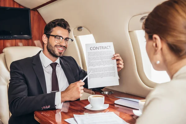 Homme d'affaires souriant montrant contrat à une femme d'affaires en avion privé — Photo de stock