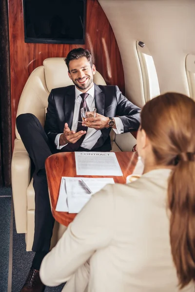 Selective focus of businessman with glass talking with businesswoman in private plane — Stock Photo