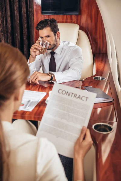 Selective focus of businessman looking at businesswoman with contract in private plane — Stock Photo