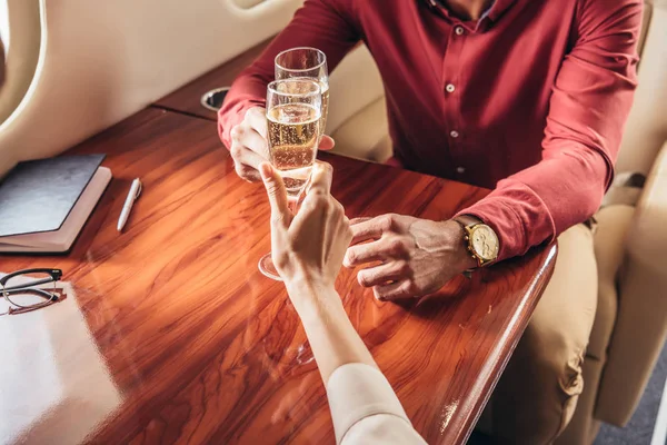 Vista ritagliata di fidanzato e fidanzata clinking con bicchieri di champagne in aereo privato — Foto stock