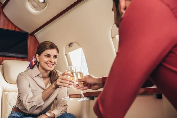 Fidanzato e sorridente fidanzata clinking con bicchieri di champagne in aereo privato — Foto stock