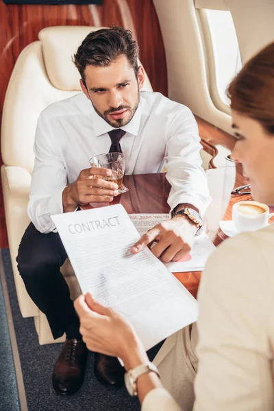 Businessman pointing with finger at contract and talking with businesswoman in private plane — Stock Photo