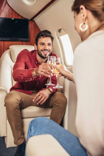 Petit ami souriant et petite amie cliquetis avec des verres de champagne dans un avion privé — Photo de stock