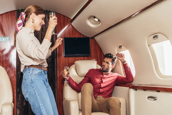 Namorado sorridente e namorada segurando copos de champanhe em avião privado — Fotografia de Stock
