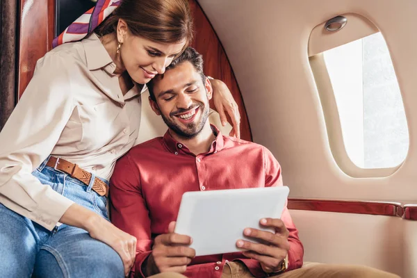 Smiling boyfriend and girlfriend looking at digital tablet in private plane — Stock Photo