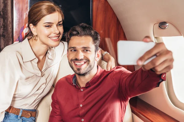 Selective focus of boyfriend and girlfriend talking selfie in private plane — Stock Photo