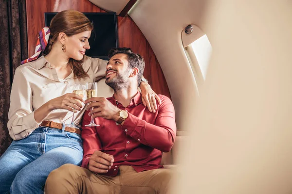 Smiling boyfriend and girlfriend clinking with champagne glasses in private plane — Stock Photo