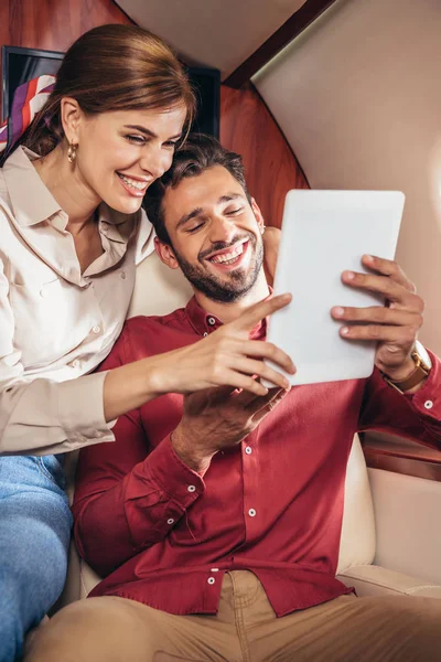 Smiling boyfriend and girlfriend holding digital tablet in private plane — Stock Photo