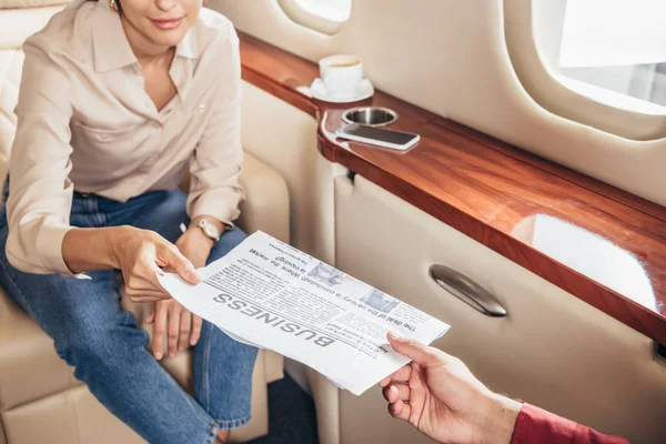 Cropped view of boyfriend giving newspaper business to girlfriend in private plane — Stock Photo