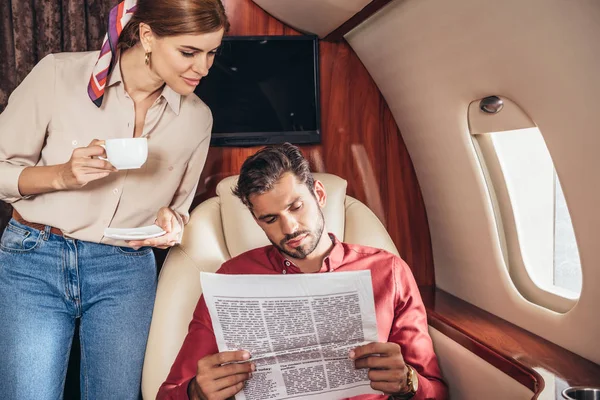 Boyfriend and girlfriend with cup reading newspaper in private plane — Stock Photo
