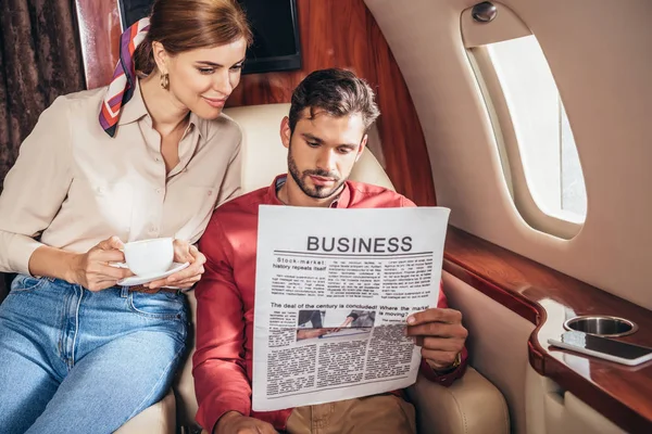 Boyfriend and girlfriend with cup reading newspaper business in private plane — Stock Photo