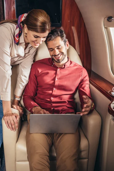 Улыбающиеся парень и девушка глядя на ноутбук в частном самолете — стоковое фото