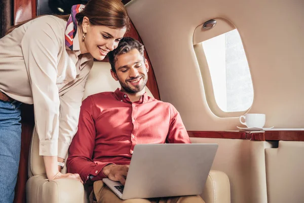 Smiling boyfriend and girlfriend looking at laptop in private plane — Stock Photo