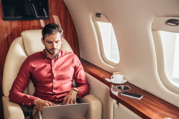 Hombre guapo en camisa usando el ordenador portátil en avión privado - foto de stock