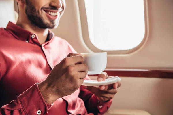 Обрізаний вид усміхненого чоловіка в сорочці, що тримає чашку в приватному літаку — стокове фото