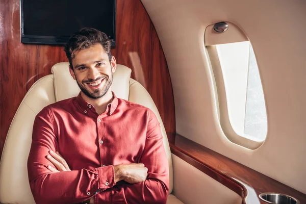 Hombre guapo y sonriente en camisa con brazos cruzados en avión privado - foto de stock