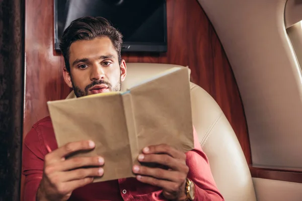 Hombre guapo en camisa libro de lectura en avión privado - foto de stock