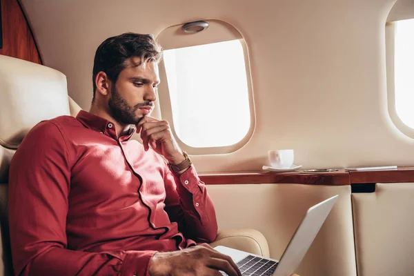 Hombre guapo en camisa usando el ordenador portátil en avión privado - foto de stock