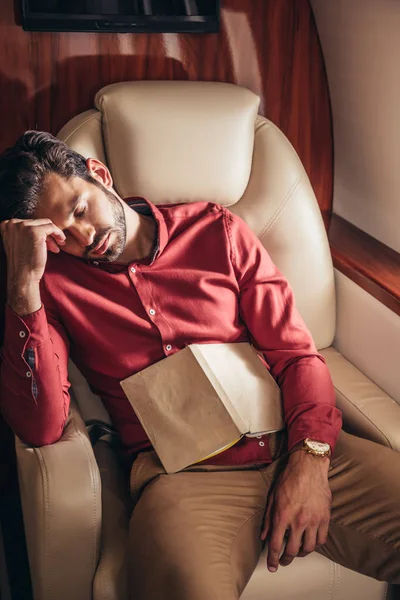 Hombre guapo en camisa durmiendo con libro en avión privado - foto de stock