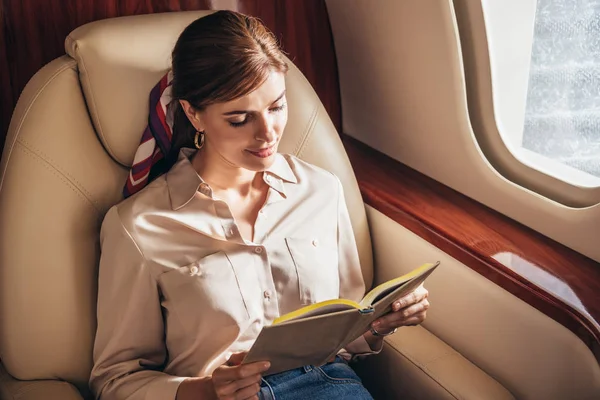 Attractive woman in shirt reading book in private plane — Stock Photo