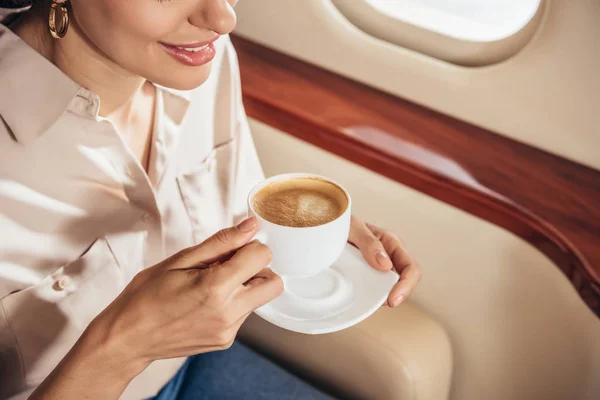 Cropped view of smiling woman in shirt holding cup of coffee in private plane — Stock Photo