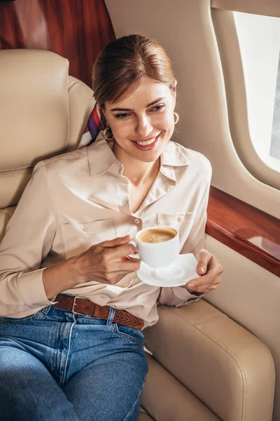 Lächelnde Frau im Hemd mit Tasse Kaffee im Privatflugzeug — Stockfoto